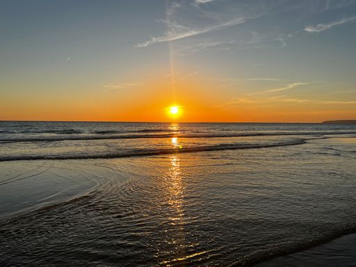 A scenic shot of the sun shining over a calm sea on a quiet summer day at sunset