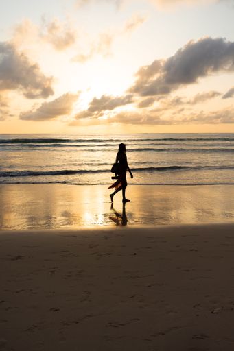A vertical shot of the silhouette of a woman walking along the beach at sunset.