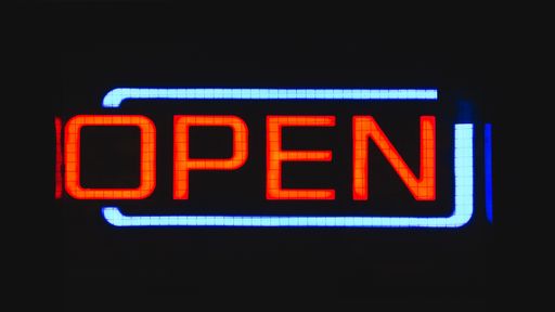 A closeup shot of an Open sign lighting up its surroundings in the middle of the night
