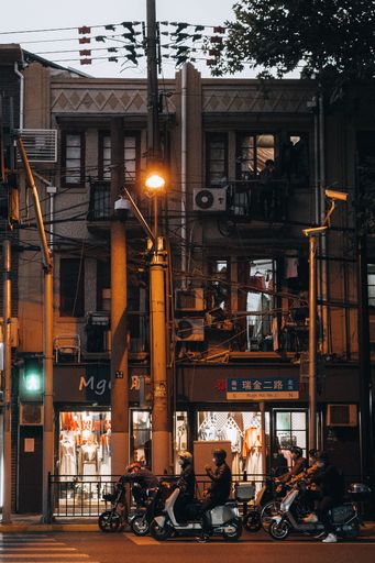 A vertical shot of people driving scooters in the streets of an old Shanghai neighborhood in the evening