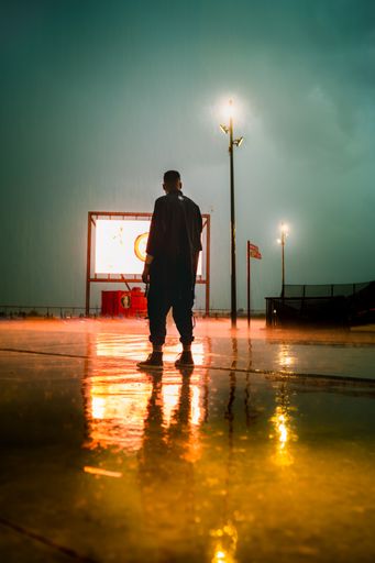 A vertical shot of a man standing in the street during the rain at night