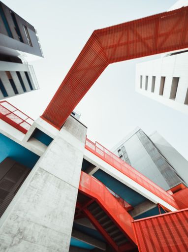 A vertical shot of a modern building with a red staircase and bridge