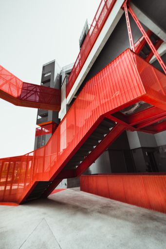 A vertical shot of a modern building with a red staircase and bridge