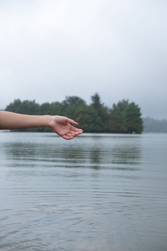 A beautiful tranquil scenery of a lake with a gentle hand of a female on the left side, vertical shot