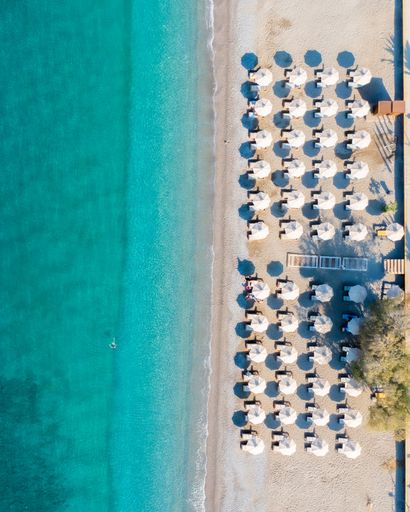 A top view of emerald beach waves washing on the sandy shore with umbrellas and sunbeds in Kalamata