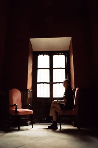 A vertical shot of a young caucasian woman sitting on a chair by a wooden door in a dark room