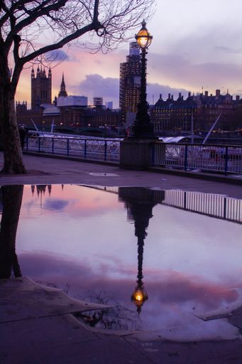 A beautiful shot of the reflection of a lamppost on a puddle with Big Ben in the background at sunset