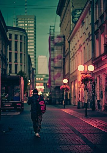 A vertical shot of a person walking in the city at dusk with lit lanterns