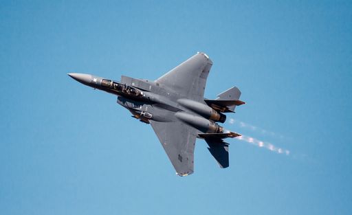 A USAF F-15E Strike Eagle fighter jet flying with afterburners in blue sky