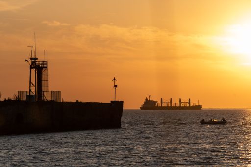 A big cargo ship, a small boat and an old pier can be seen at Uruguay River, Conchillas, Uruguay