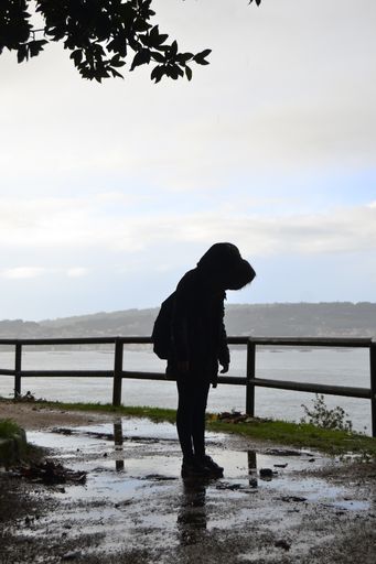 A vertical shot of a person in a hooded jacket standing near a lake
