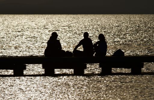 A beautiful shot of silhouettes of people hanging around on a wooden dock over a pier at sunset