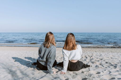 Two female friends sitting on a beach looking out at the vast ocean, enjoying the view and each other's company