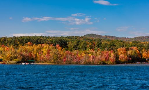 A landscape scene of Lake George coast with forest autumn trees and boats under blue sky