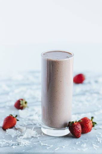A closeup shot of a delicious chocolate shake in a tall glass cup surrounded by strawberries