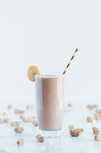 A closeup shot of a delicious cookie shake in a tall glass cup surrounded by peanuts