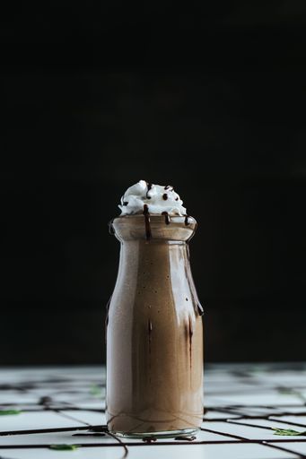 A closeup shot of a cute mini glass bottle of chocolate milkshake topped with whipped cream