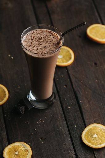 A closeup shot of a tall glass cup of chocolate milkshake with a metal straw on a wooden surface