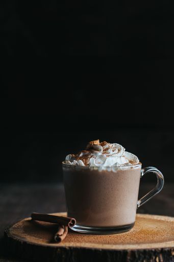 A vertical closeup shot of a glass of hot chocolate on a wooden board, with cream on top