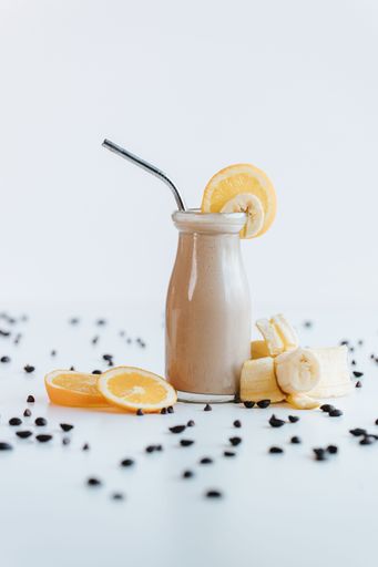 A closeup shot of a cute mini glass bottle of orange milkshake decorated with orange and banana