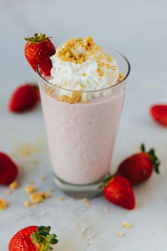 A vertical closeup shot of a glass of a strawberry milkshake surrounded by strawberries