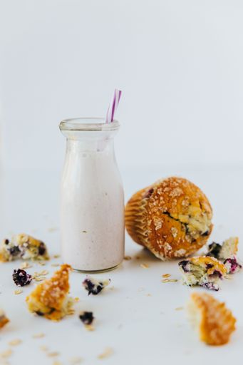 A vertical closeup shot of a glass of a protein shake with a muffin on the side