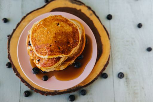 A top view shot of pancakes on top of each other with blueberries on the plate, with maple syrup on it