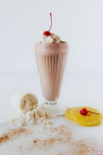 a vertical closeup shot of a  glass of Chocolate Protein Shake with Cherry against white background
