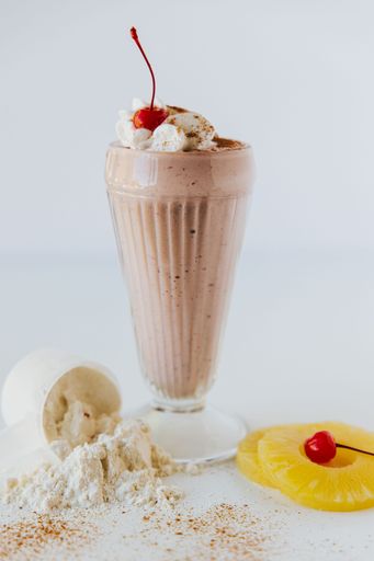 a Vertical closeup shot of a  glass of Chocolate Protein Shake with Cherry against white background