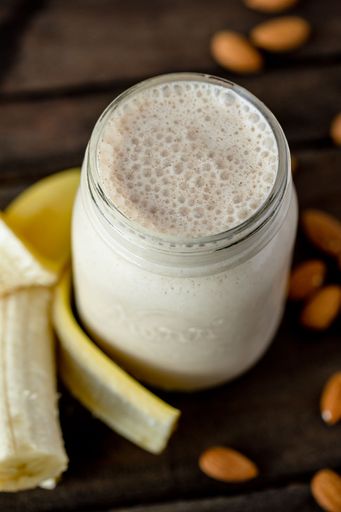 a Selective focus vertical high angle closeup shot of a banana almond milkshake on a wooden surfa