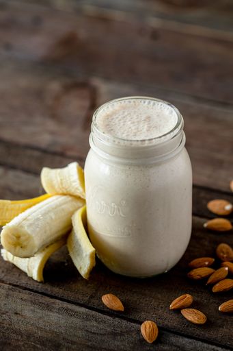 a Selective focus vertical high angle closeup shot of a banana almond milkshake on a wooden surface