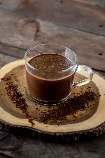 a Vertical high angle shot of dark chocolate milkshake in a  glass mug on wooden surface