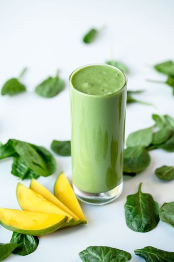 a vertical shot of a green healthy milkshake in a  glass mug on white surface