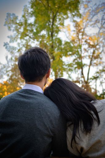 A vertical shot of a girl with her head on his boyfriend's shoulder in a park