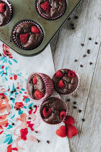 A vertical shot of the brown muffins with raspberries and chocolate