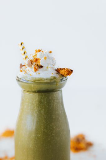 A vertical closeup shot of a glass of green smoothie with whipped cream on it on a white surface