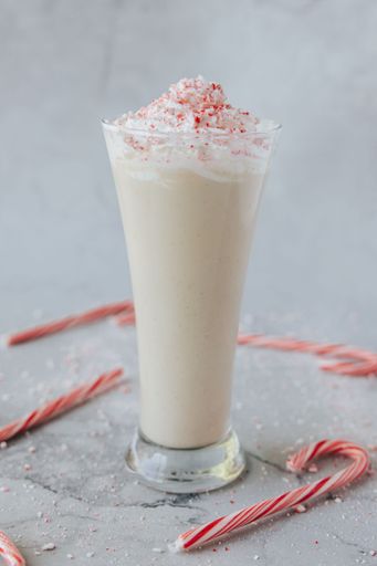 A closeup shot of a glass of candy cane shake served on a table surrounded by red and white candy canes
