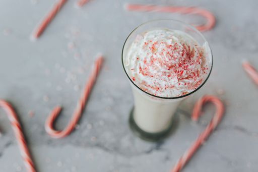 A top view of a glass of candy cane shake, sprinkled with candy cane crumbs, with blurred red and white candy canes in the background