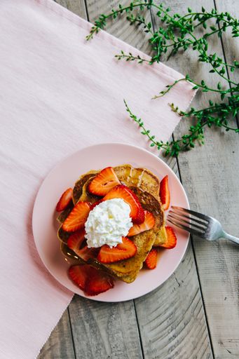 A top view of french toast with whipped cream and strawberries on a wooden table