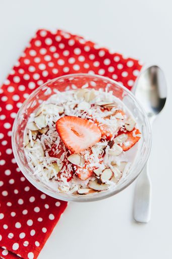 A vertical shot of appetizing Oats with Strawberries in a bowl with a red decorative napkin and a spoon on the side