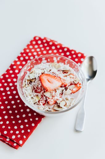 A vertical shot of appetizing Oats with Strawberries in a bowl with a red decorative napkin and a spoon on the side
