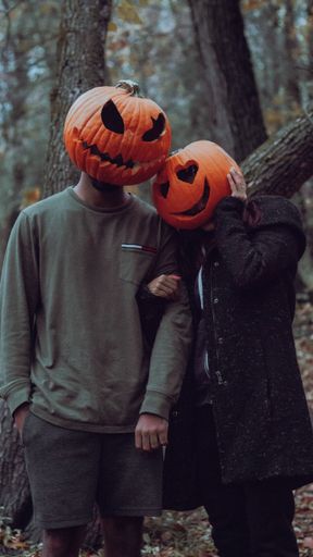 A vertical shot of a couple wearing curved pumpkins on their heads