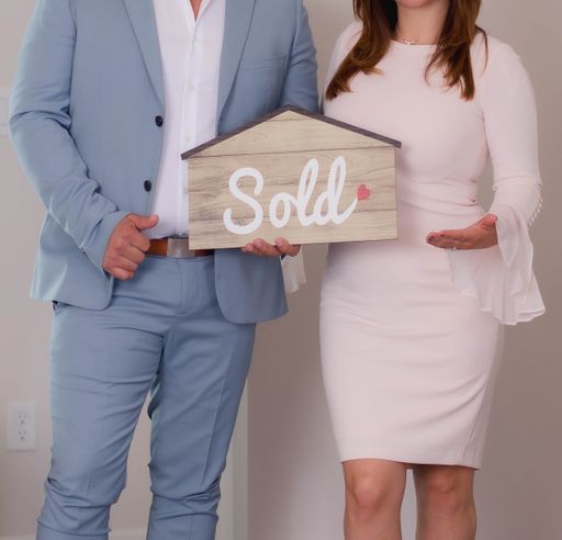 A couple holding a house-shaped paper with the word sold printed on it