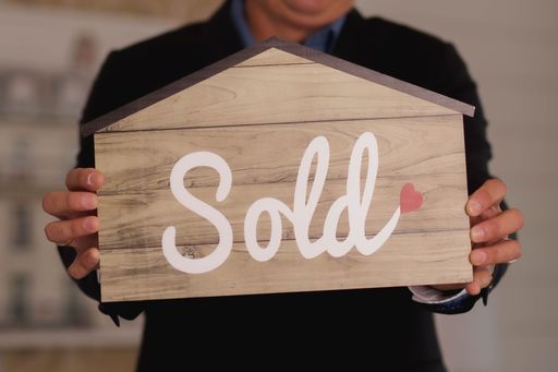 A person holding a sold sign in the shape of a house - concept of sale
