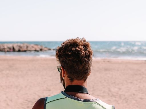 A back view of a male in a face mask and sunglasses at the beach