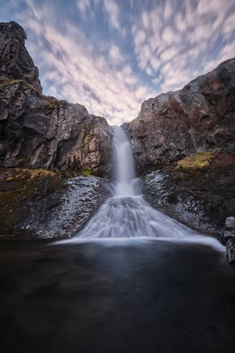 A vertical long exposure shot of the Klifbrekku Waterfall in Iceland