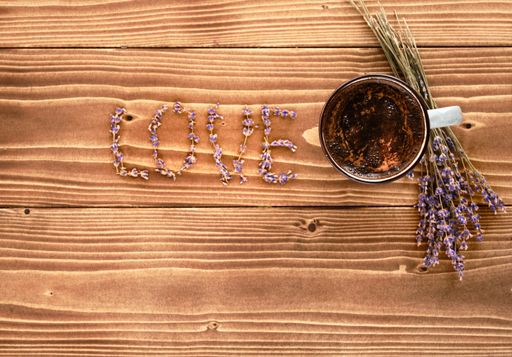 A top view of a cup of tea and the word LOVE made of lavender petals on a wooden surface