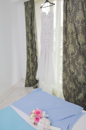 A vertical shot of a white wedding dress hanging from a curtain rod