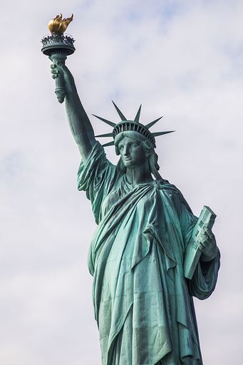 A vertical shot of the statue of Liberty in New York City on a cloudy sky background