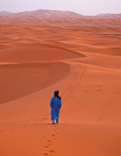 A vertical back view of a male walking in the desert, Morocco, Africa